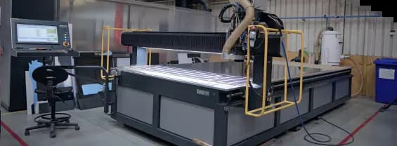 A large CNC routing machine with an attached control panel terminal in a workshop setting.