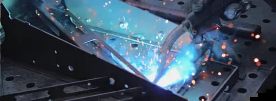A close-up view of a welding torch joining metal parts, producing a bright blue flash and flying sparks.