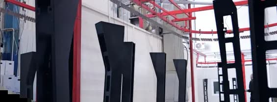 Finished black metal components hanging from an automated overhead conveyor line inside a factory.