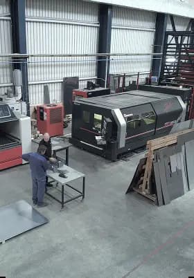 High-angle view of workers operating large industrial CNC laser cutting machines inside a manufacturing factory floor