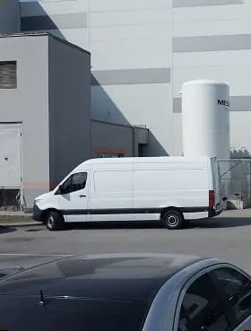A white delivery cargo van parked outside an industrial warehouse facility ready for logistics and shipping